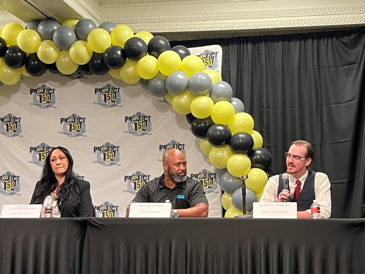 A NNSS employee speaks sitting next to two panelists.