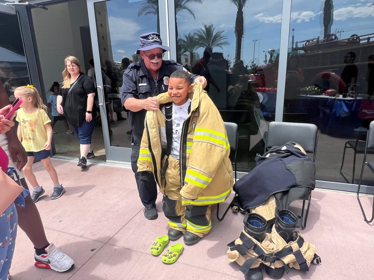 A NNSS firefighter puts a firefighter's suit on a boy.