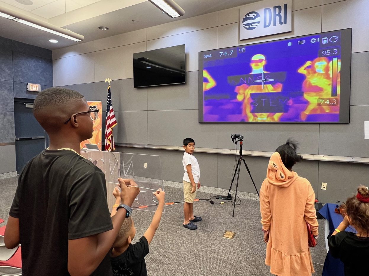 Students hold up signs that read "NNSS" and "STEM" to an infrared camera.