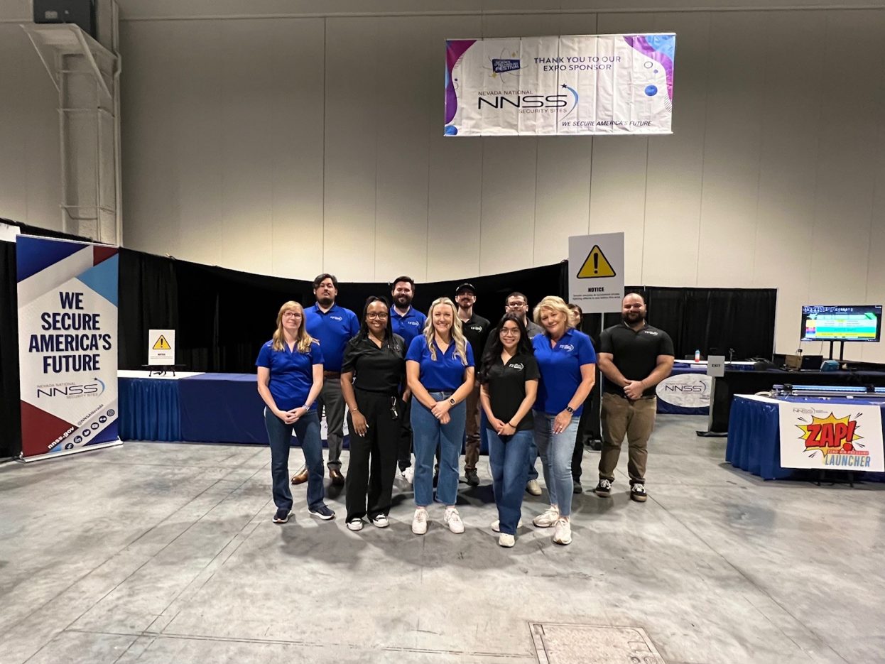 A group of NNSS employees smile in an exhibition hall.