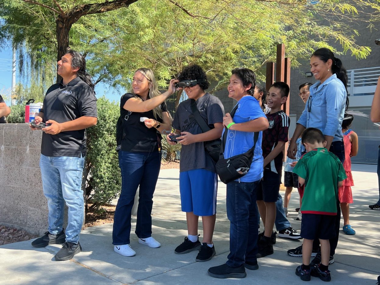 Students smile while operating a drone outside.