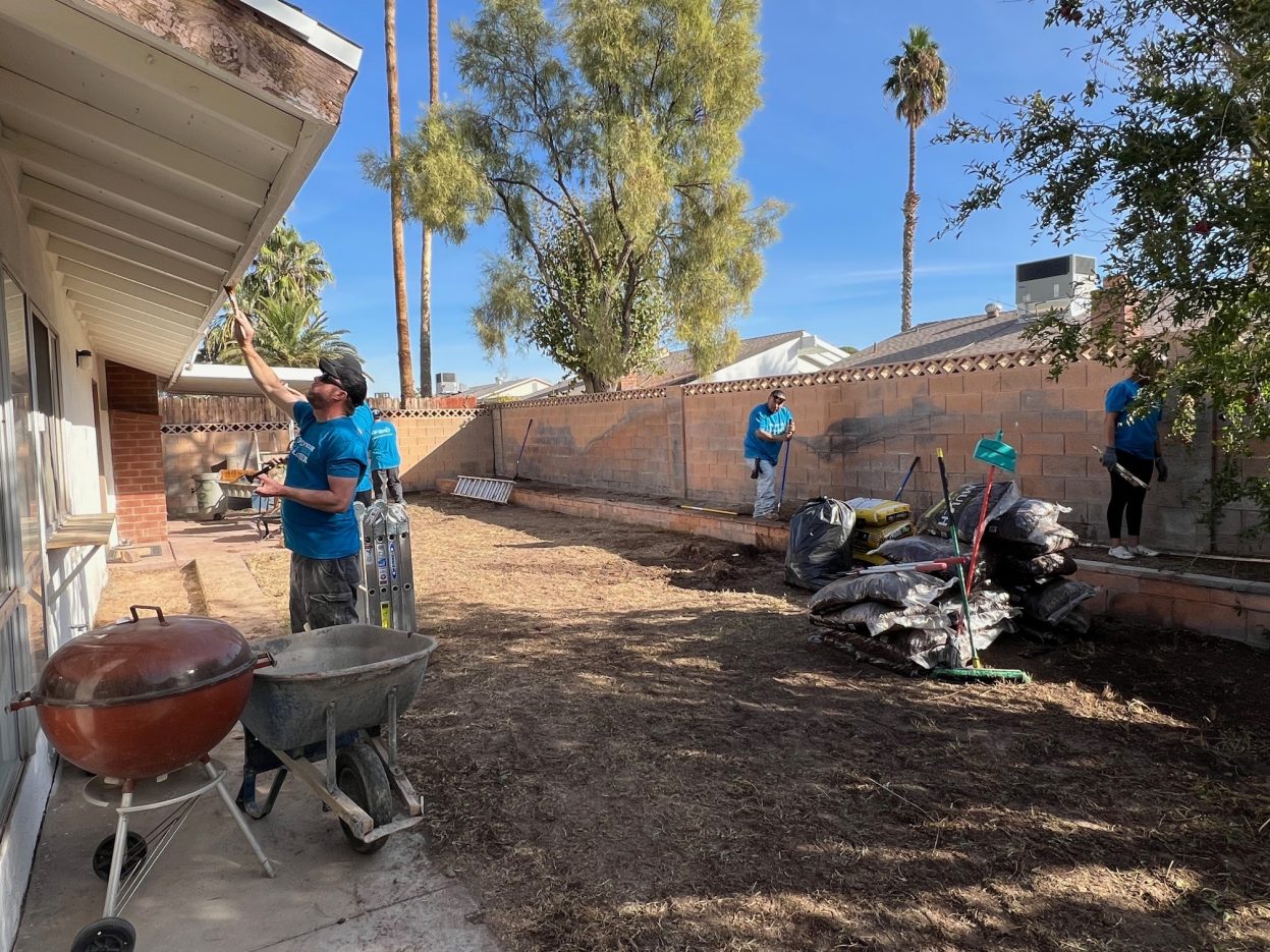 Volunteers paint trim and prepare flowers for planting at a property.