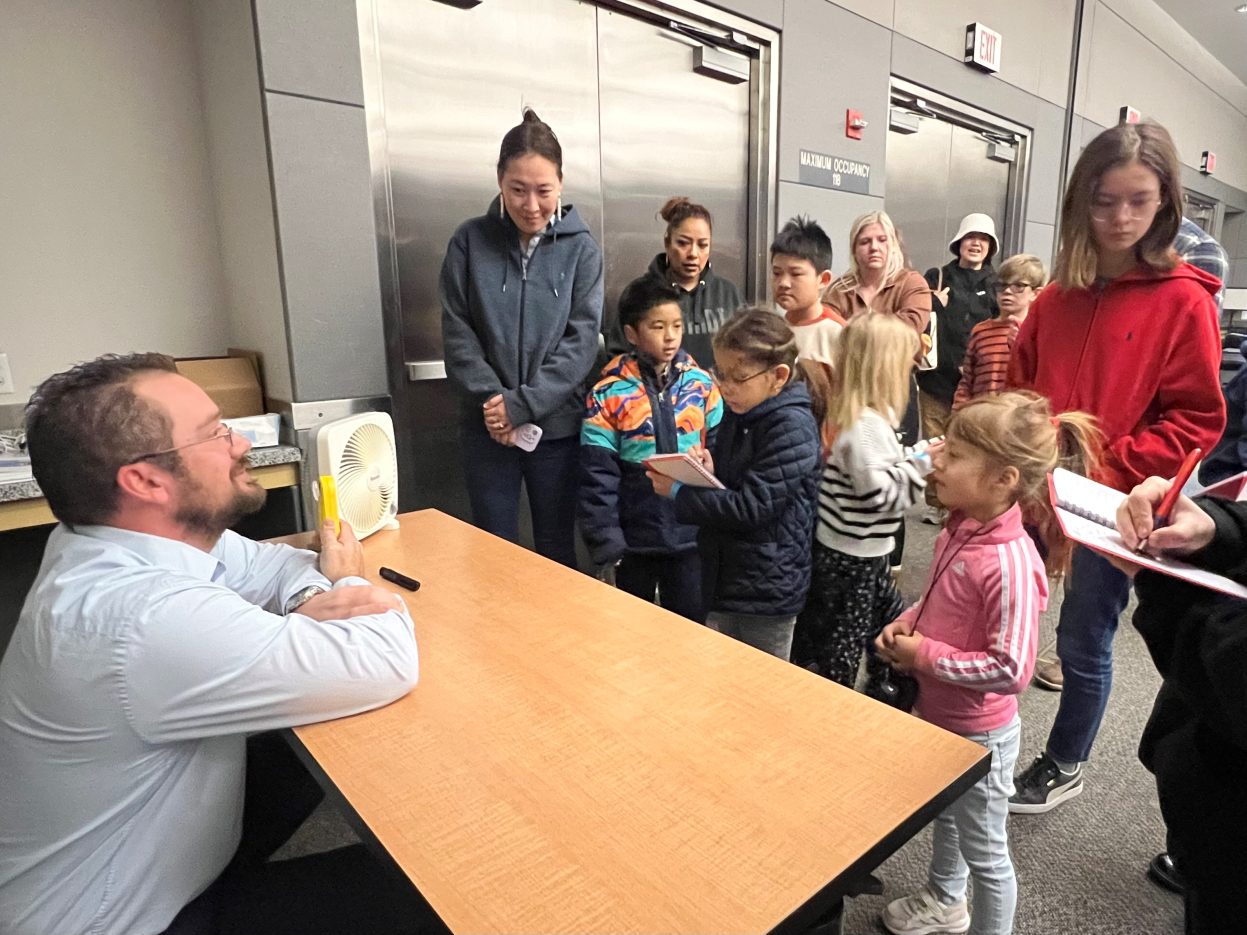 A meteorologist demonstrates a temperature reading in front of a fan while students take notes,