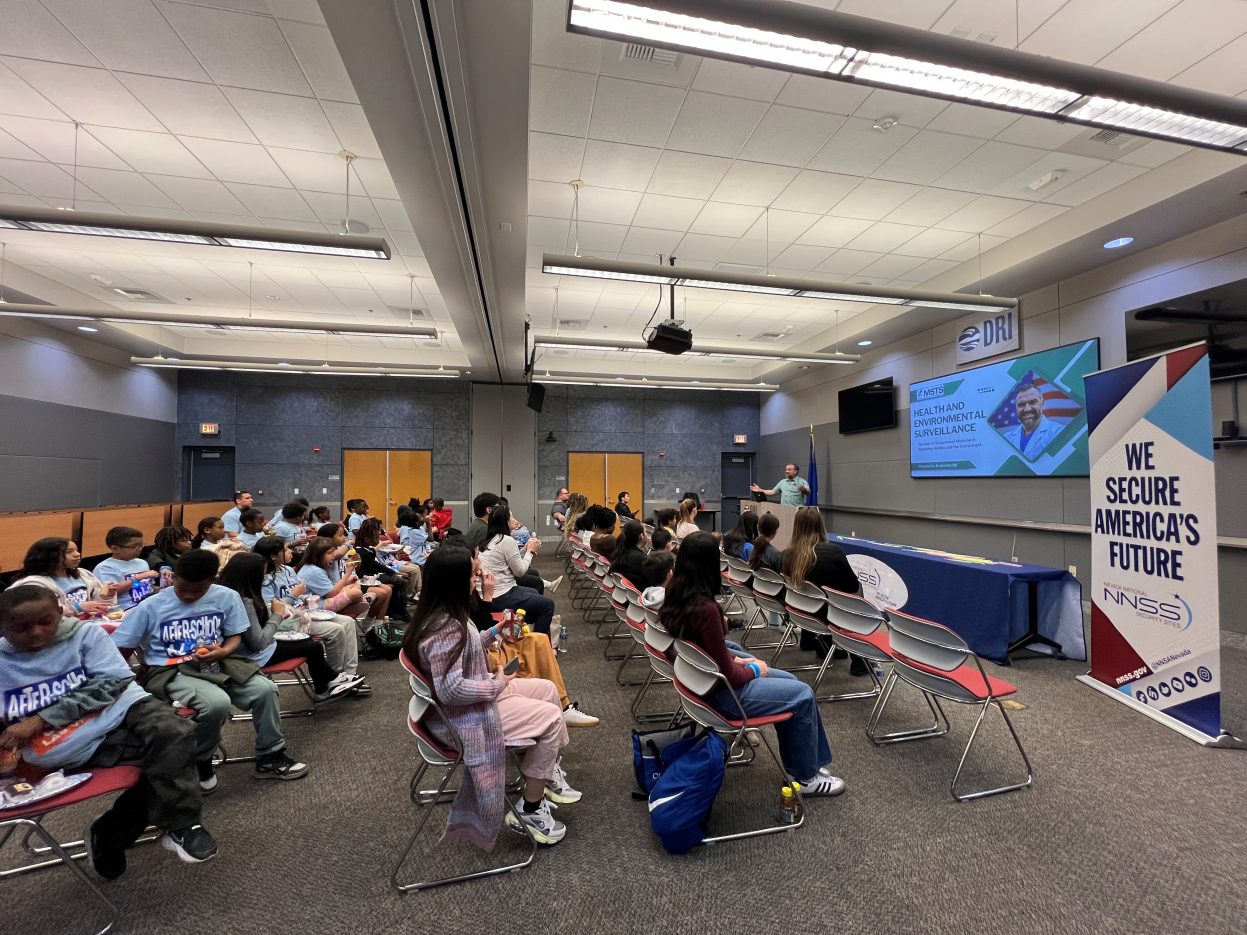 Students seated in auditorium chairs watch a doctor give a presentation.