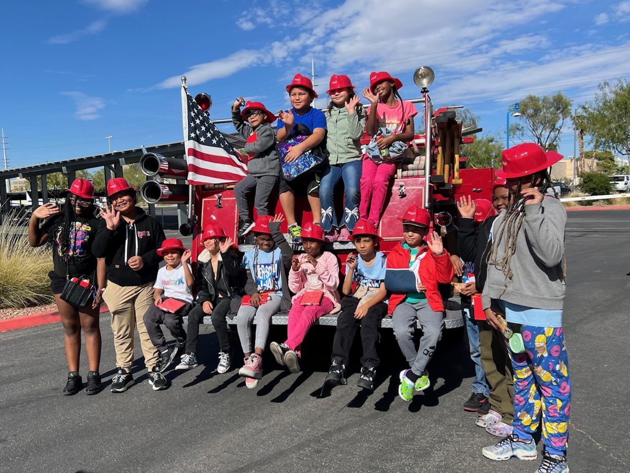 A group of students wear red firefighter hats while waving.