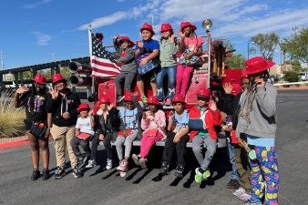 A group of students wear red firefighter hats while waving.