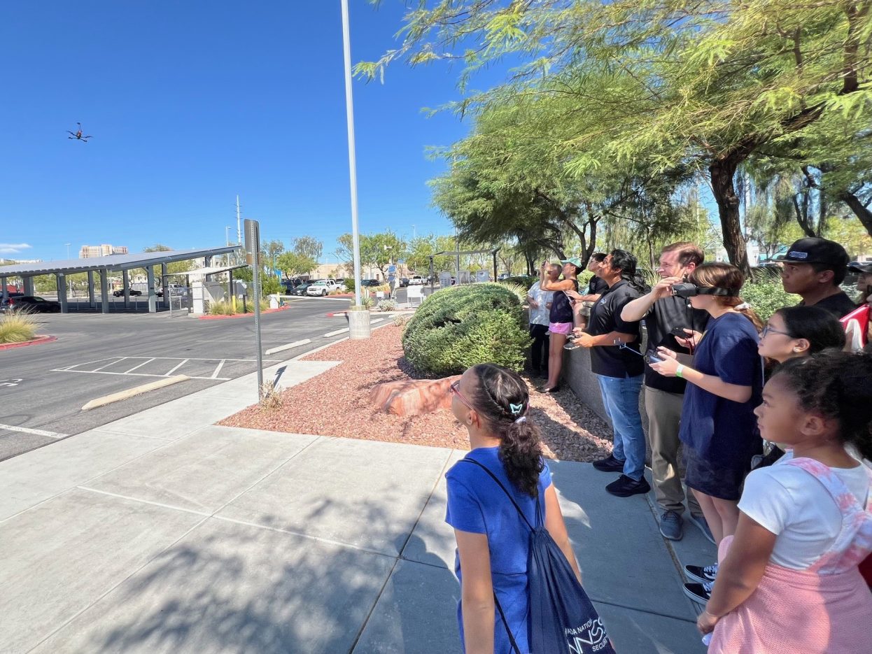 A group watches as a student operates a drone outside via a transmitter.