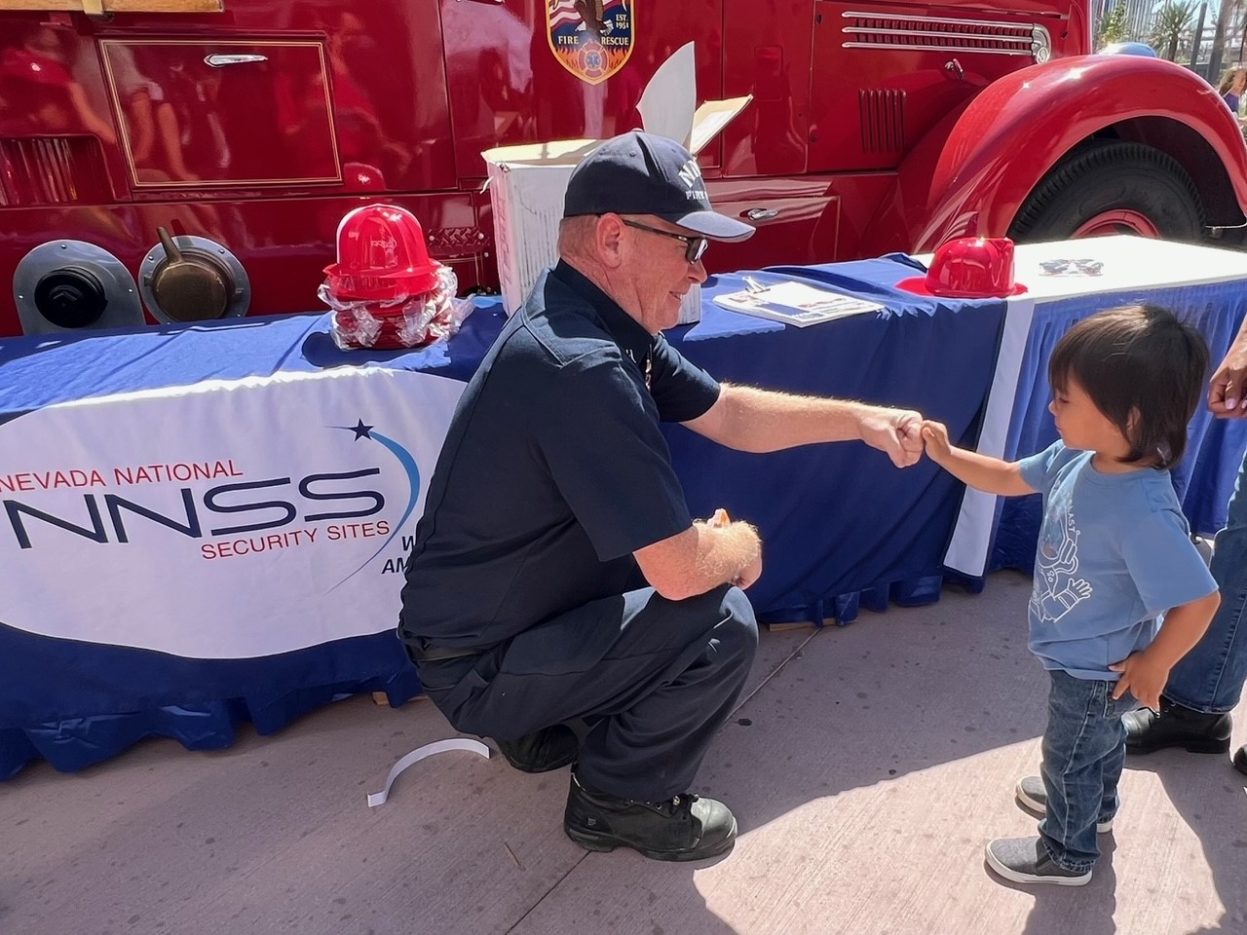 A NNSS firefighter meets a boy next to a red fire engine.