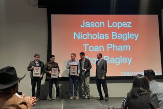 Students accept a framed award on stage as audience members applaud.