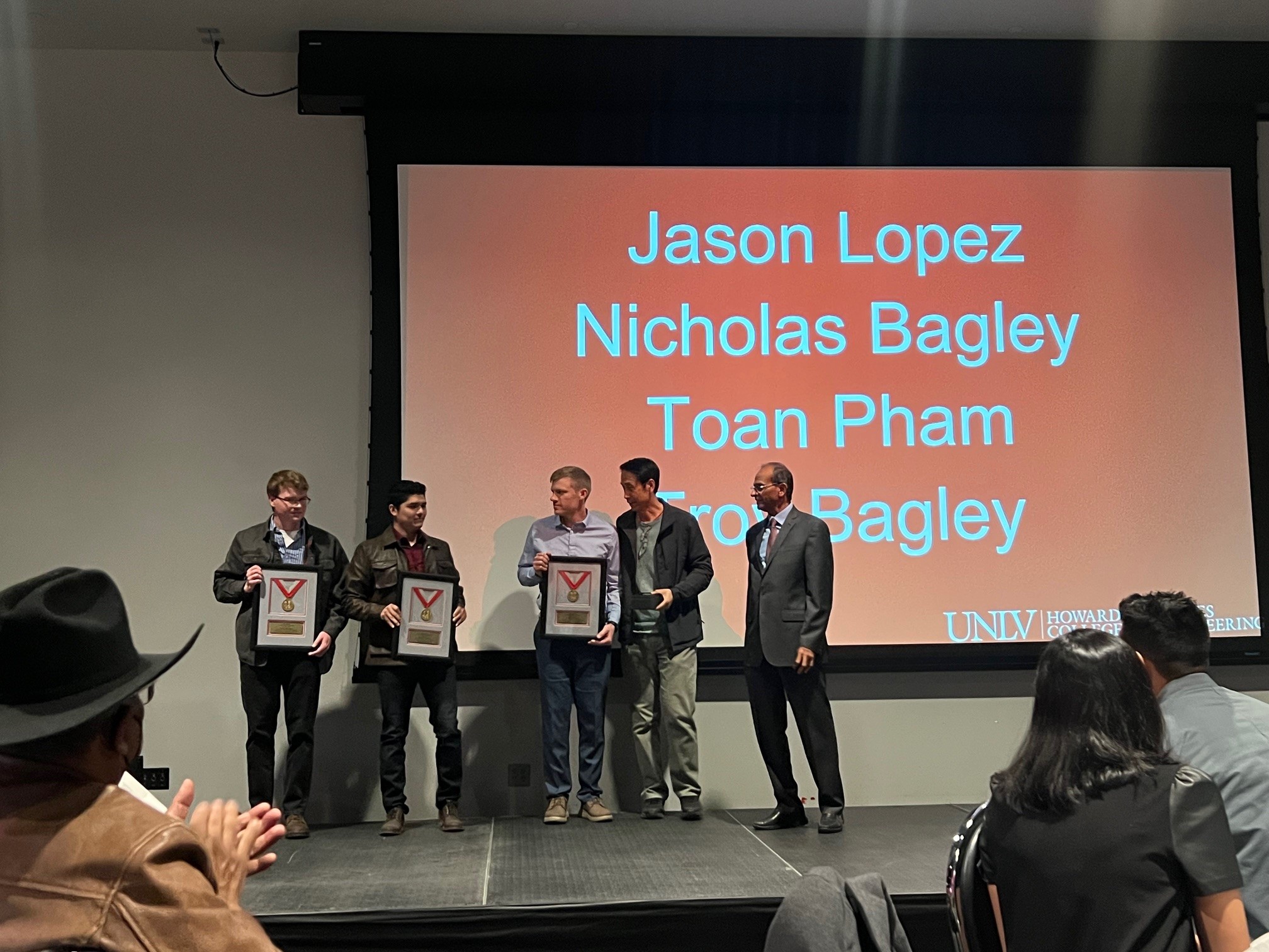 Students accept a framed award on stage as audience members applaud.