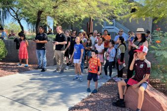 A group of students and parents watch a drone operate outdoors.