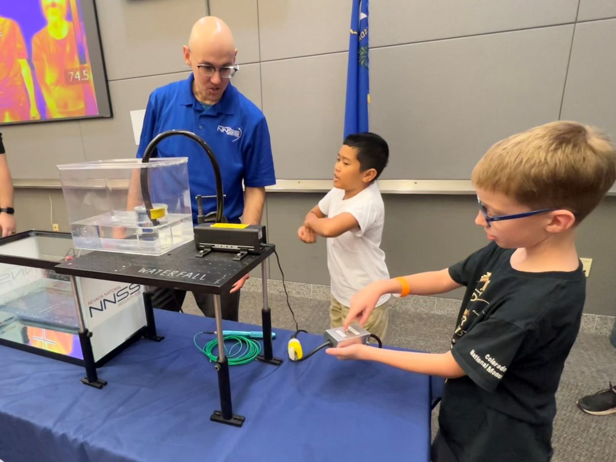 Two students interact with a NNSS scientist who is demonstrating fiber optics.