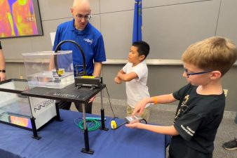 Two students interact with a NNSS scientist who is demonstrating fiber optics.