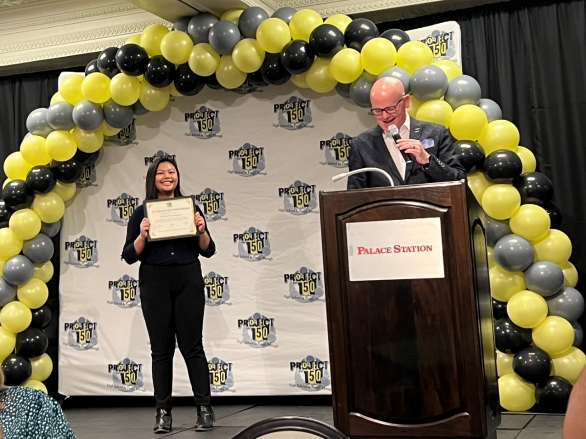 A student holds up a certificate on stage.