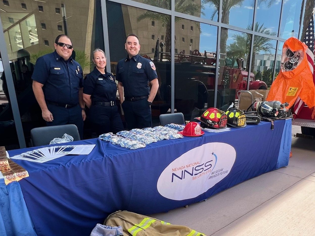 Three Fire & Rescue personnel smile at an exhibition display.