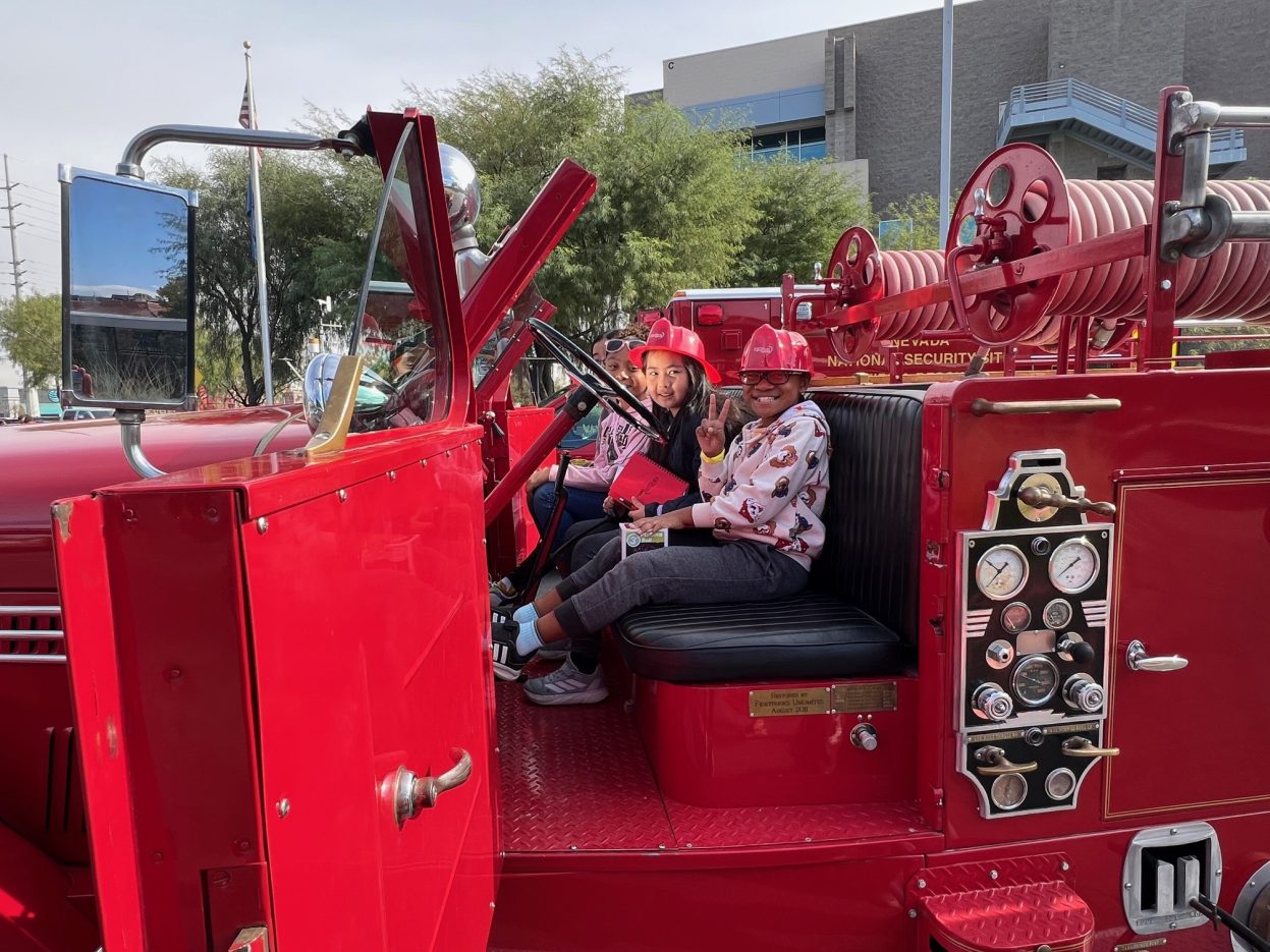 Students wearing ref firefighter hats smile from the 1950 Seagrave's seat.