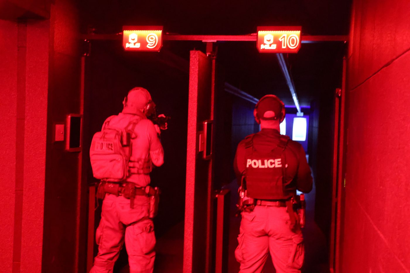 Two men in tactical gear stand in lanes with red lighting.