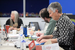 two female and one male member of the NSSAB sitting at a table with papers and laptops working