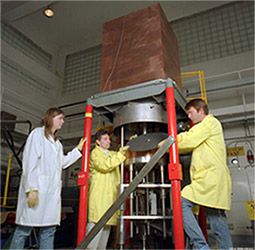Three employees in laboratory coats prepare the Comet criticality assembly machine.