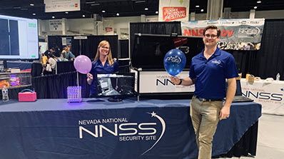NNSS employees holding balloons at table with computer monitor on it