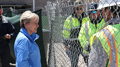 Energy Secretary Jennifer Granholm stands near fence talking to workers in hard hats