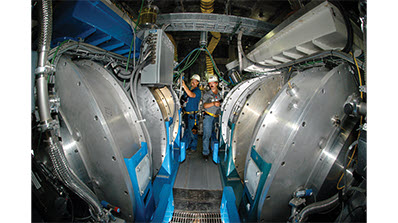 silver and blue Cygnus dual axis X-ray machine underground at U1a, two men in hard hats in background