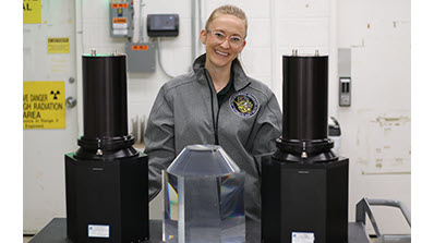 Amber Guckes in gray jacket standing behind table with three detectors on it