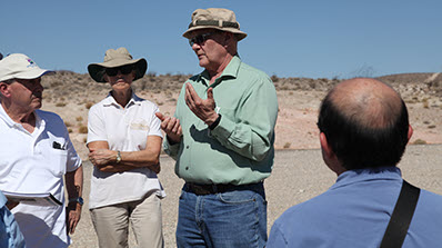 man in green shirt and hat talks to group outside at the NNSS