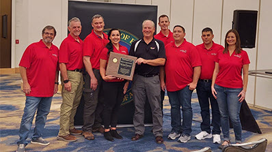 group of MSTS employees in red shirts receive award in ballroom