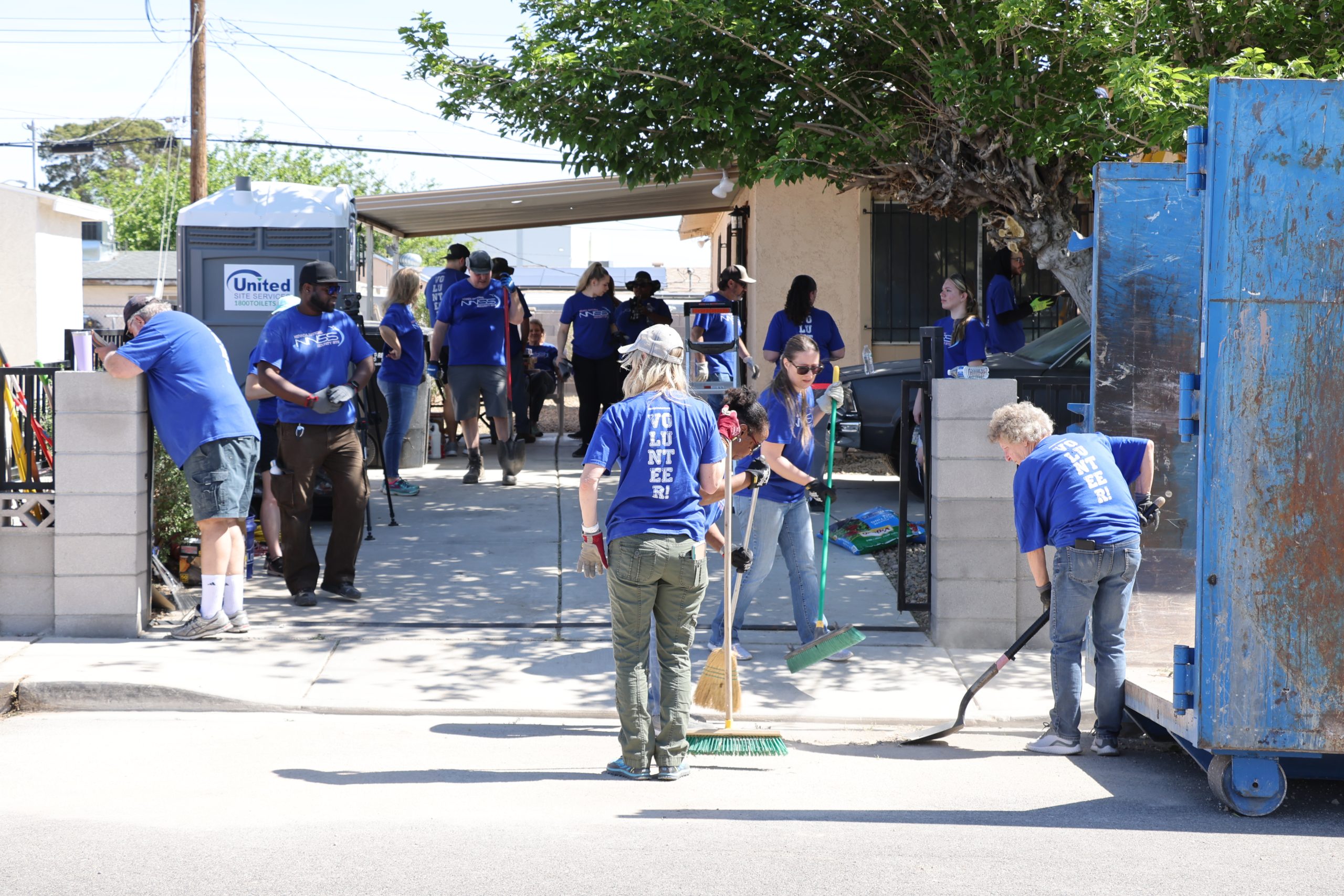 volunteers in blue NNSS shirts working outside a home sweeping and doing other yardwork