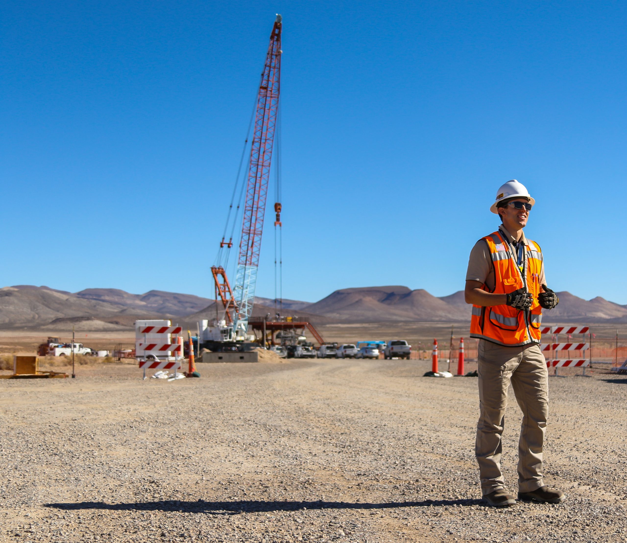 male engineer in orange vest and hard hat outside in front of a crane