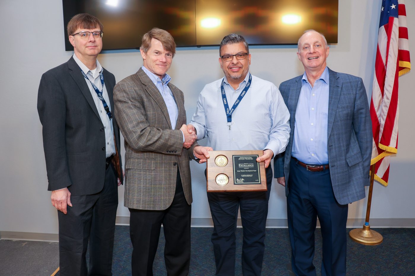 four men on stage with one in center accepting plaque and shaking hands