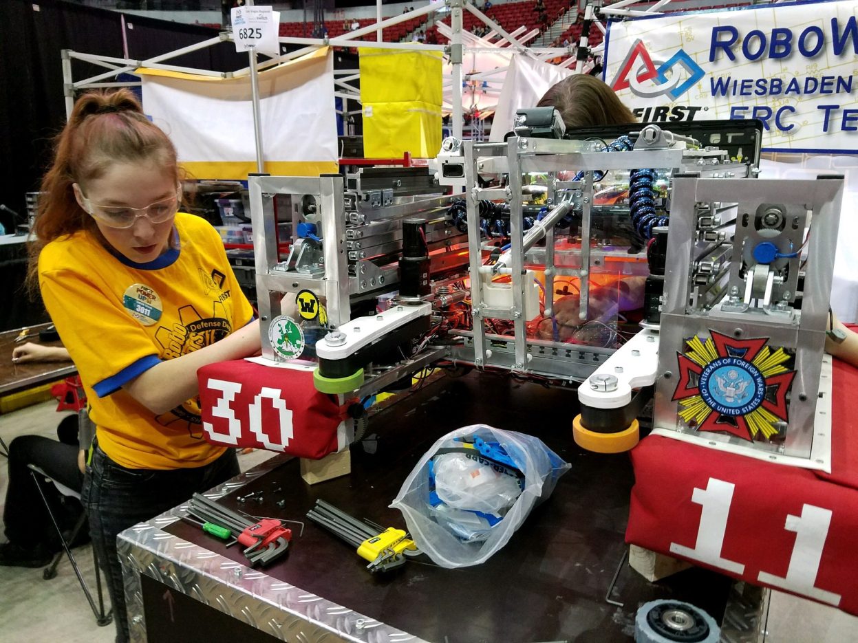 girl to left in yellow shirt working on a robot for the FIRST Robotics competition