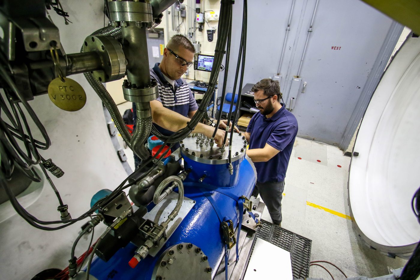 two men in blue shirts working on the target chamber at the JASPER facility