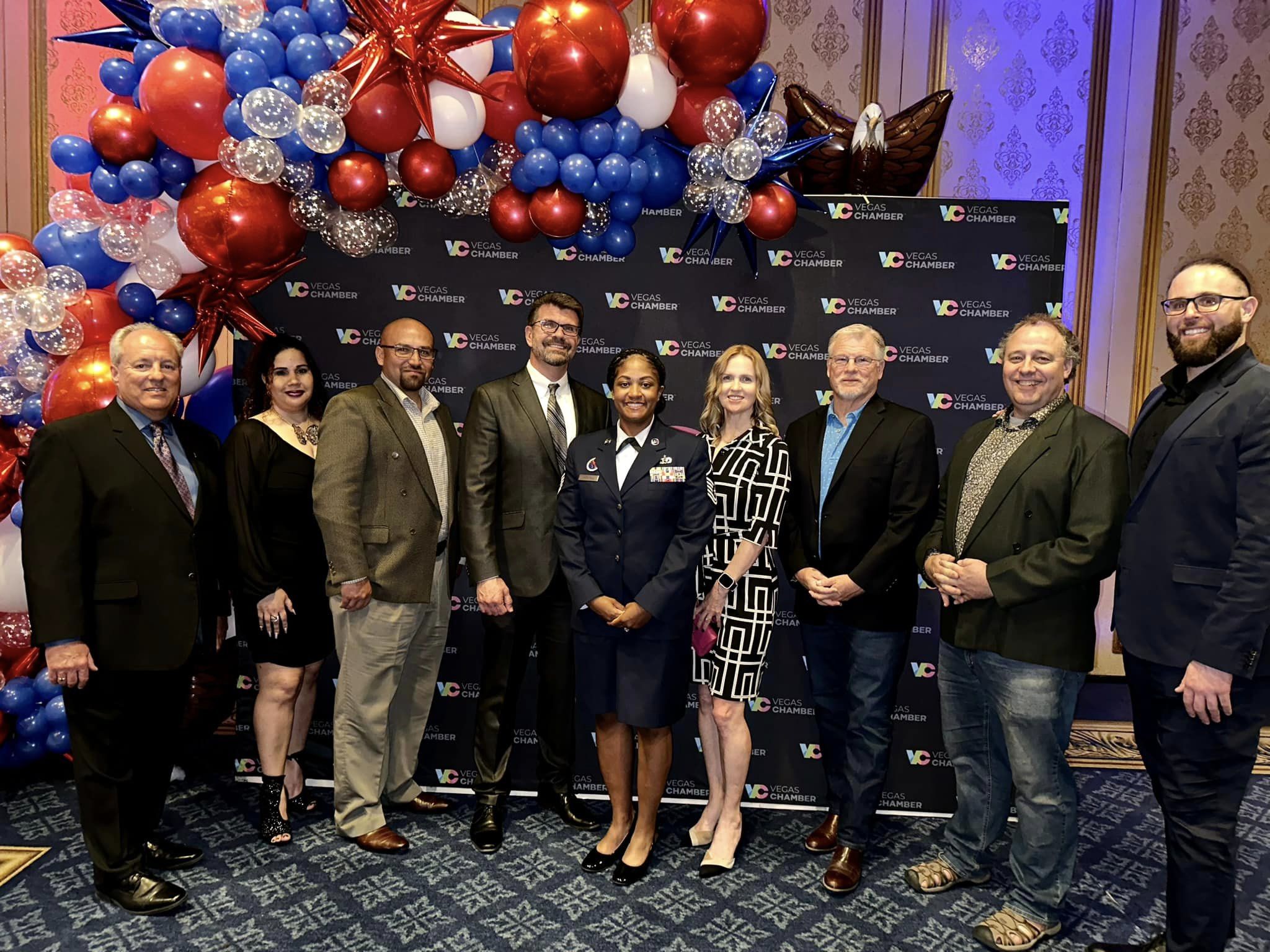 group of men and women in front of red, white and blue balloons and background at awards dinner