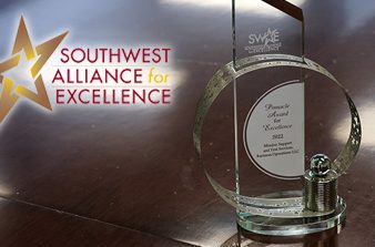 SWAE logo in top left corner with glass award sitting on dark brown table