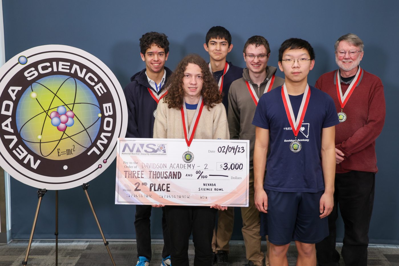 five students and a teacher pose with medals and big fake check for taking 2nd place at Nevada Science Bowl