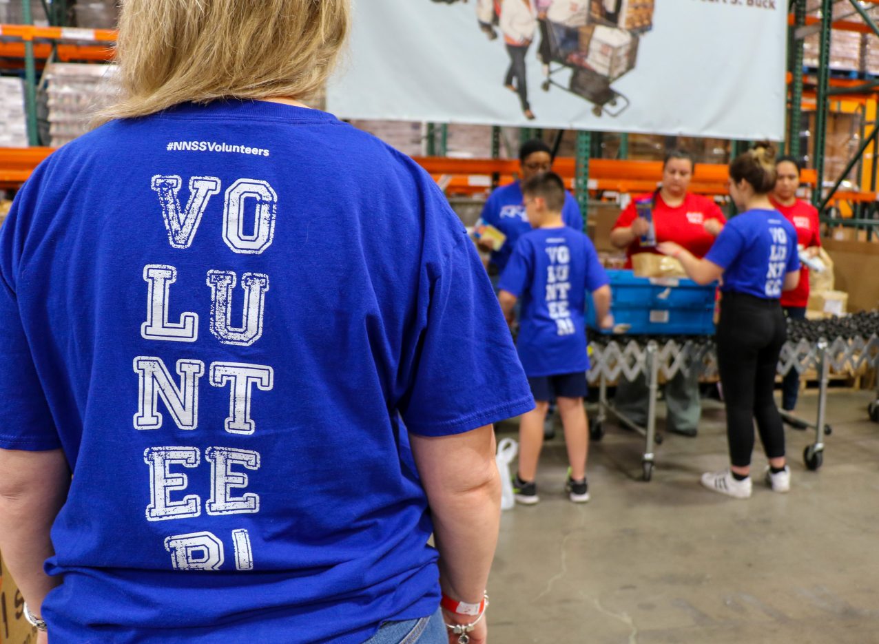 back of women in foreground showing blue NNSS volunteers shirt with other volunteers in background