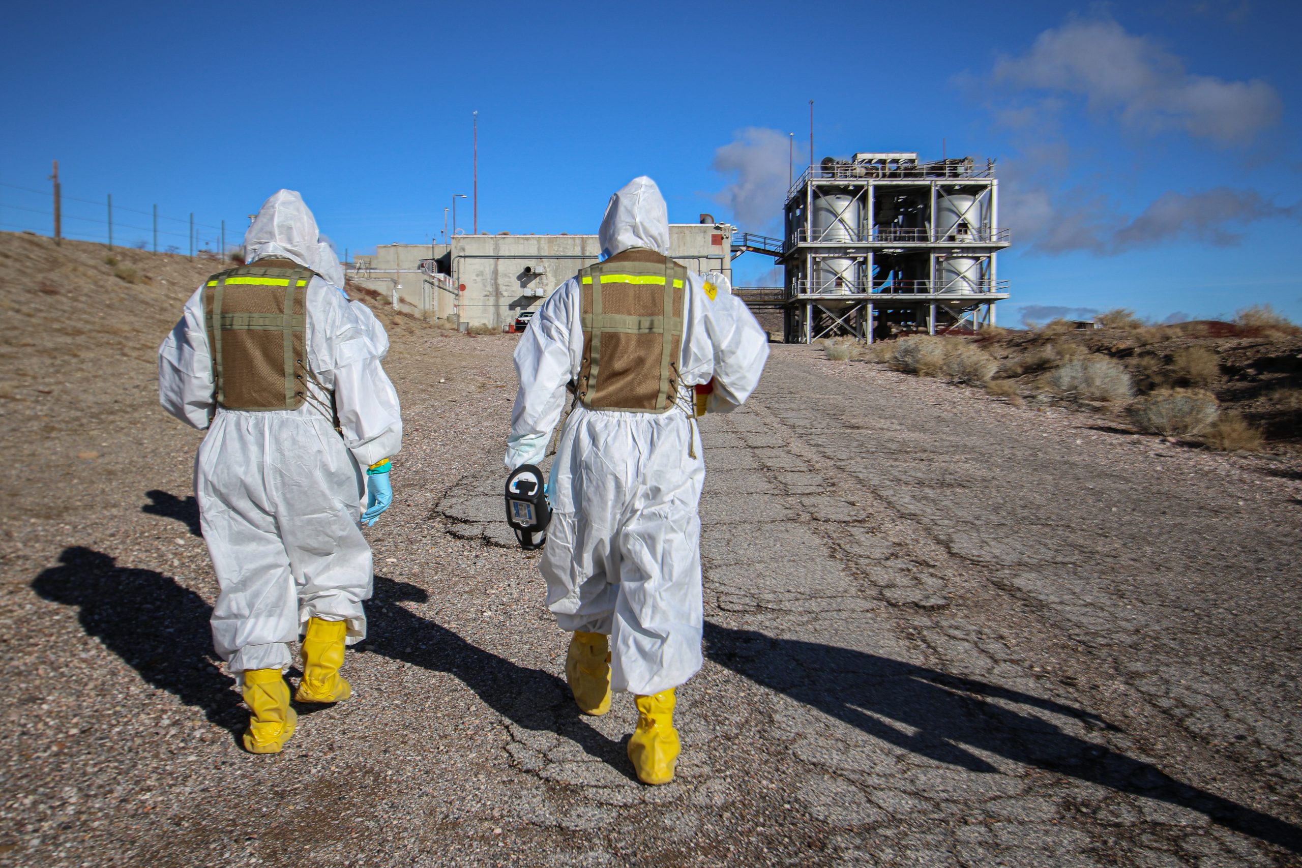 Two trainees in personal protective equipment train approach a building structure.