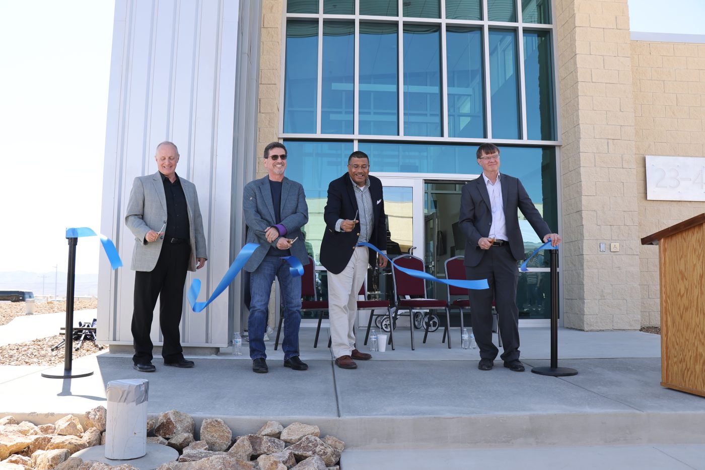 four men in front of new building cutting a blue ribbon