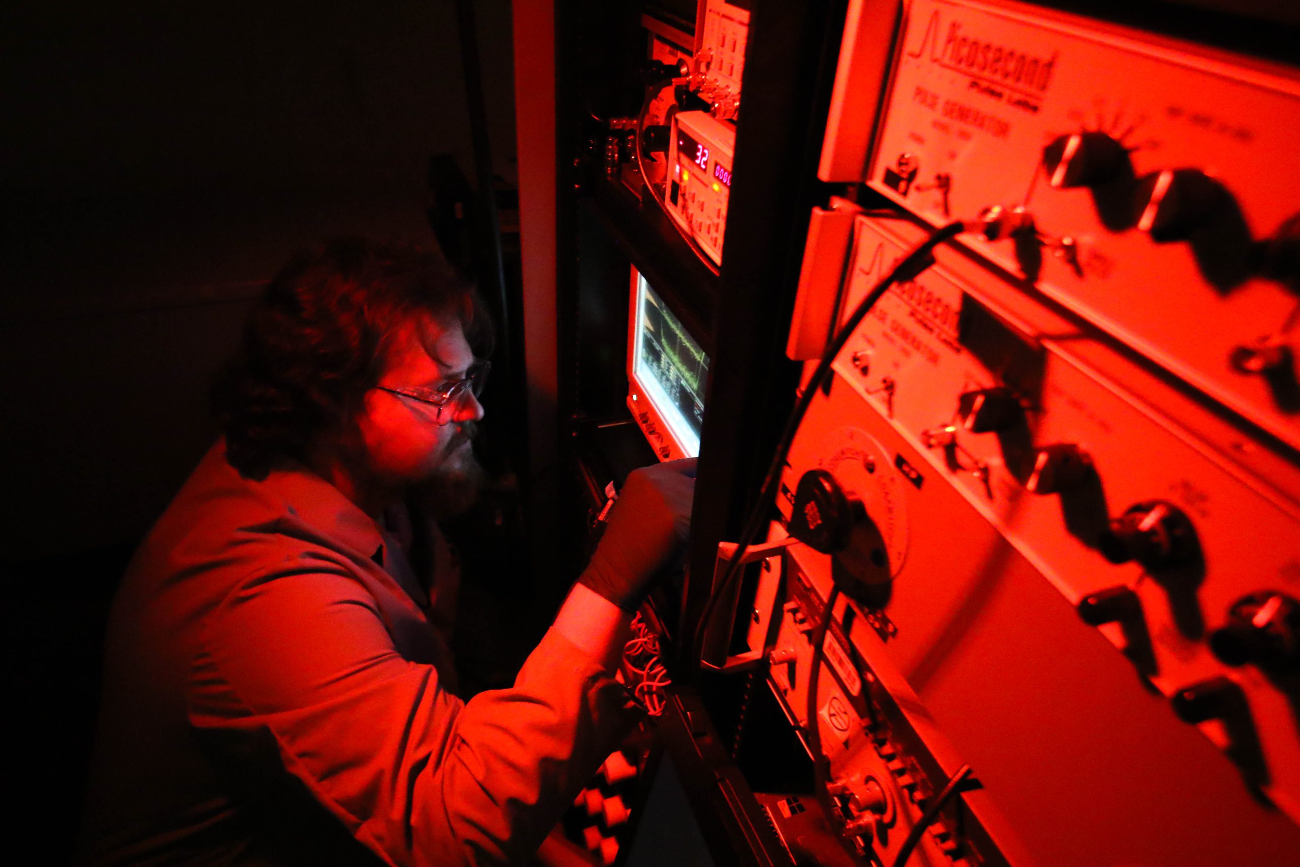 A man makes machine adjustment in a room lit with a red glow.