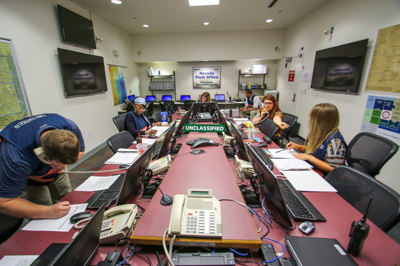 people sitting around a table in an operations center talking on phones and to each other during an emergency