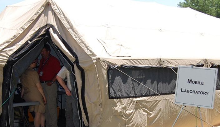Individuals speak inside a tent structure that is used for mobile laboratory capabilities.