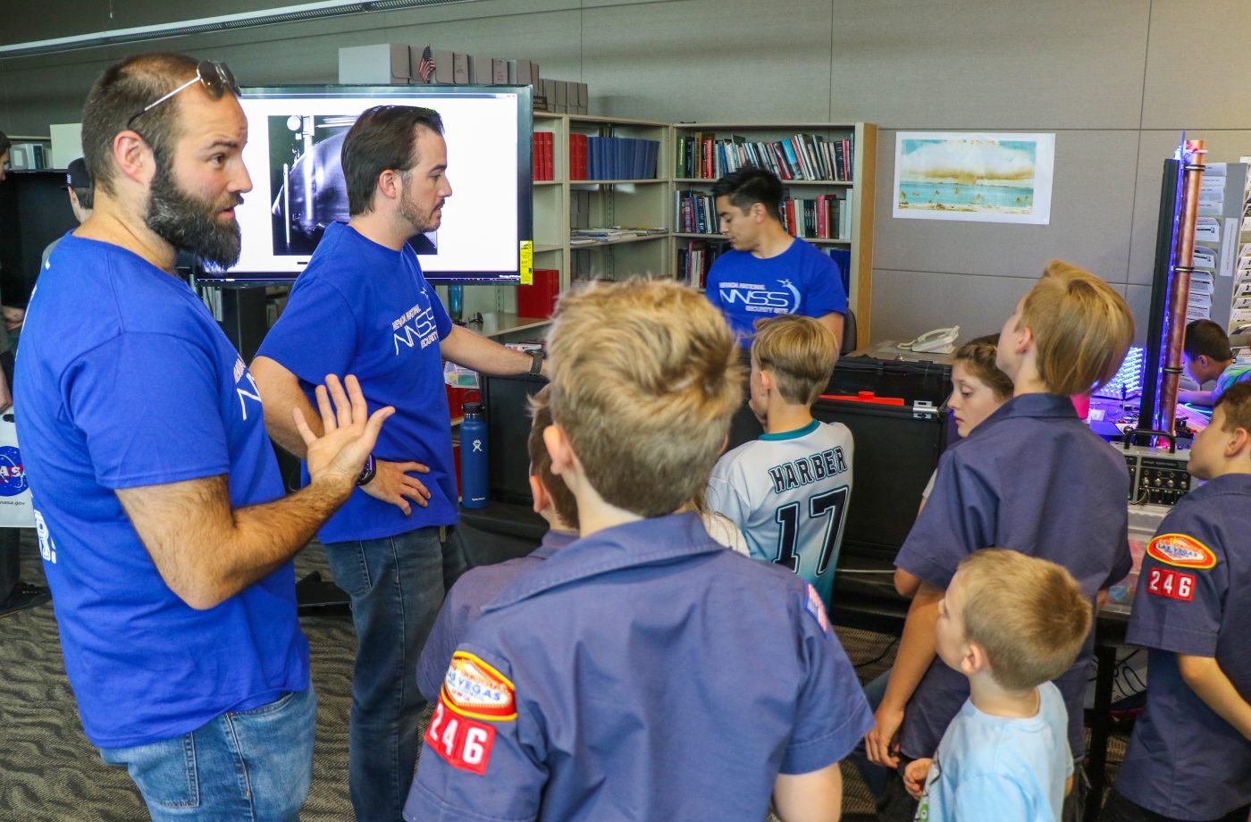 NNSS volunteers in blue shirts talking to a group of Boy Scouts during a community event