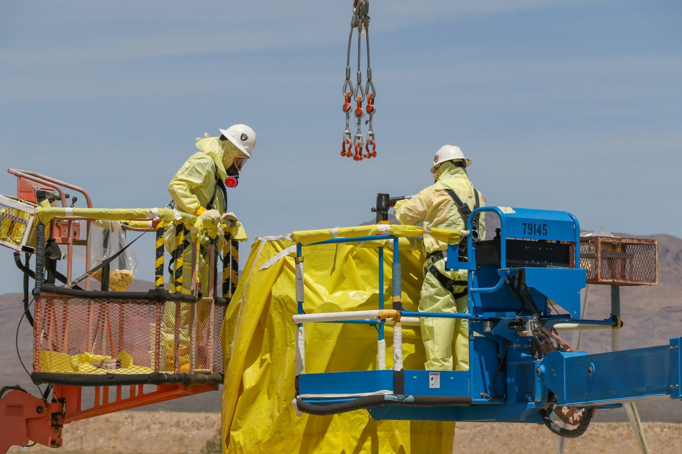 Two NNSS employees in personal protective equipment prepare waste for disposal from lift equipment.