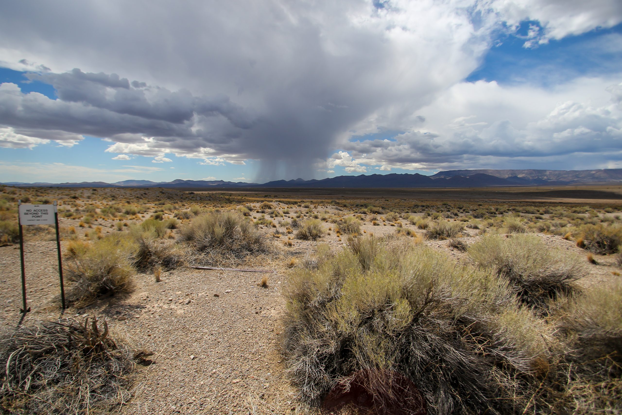 landscape image of desert with rain clouds and mountains in background