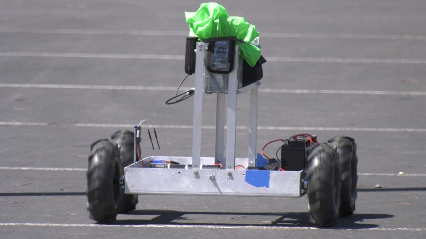 a small robot with bright green on top sits in parking lot