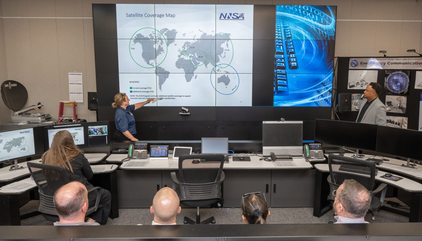 A presenter gestures to a map of the world in front of several officials inside the Emergency Communication Network.