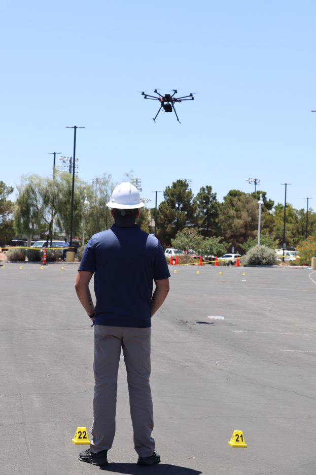 male in blue shirt and white hard hat pilots a UAS over a parking lot