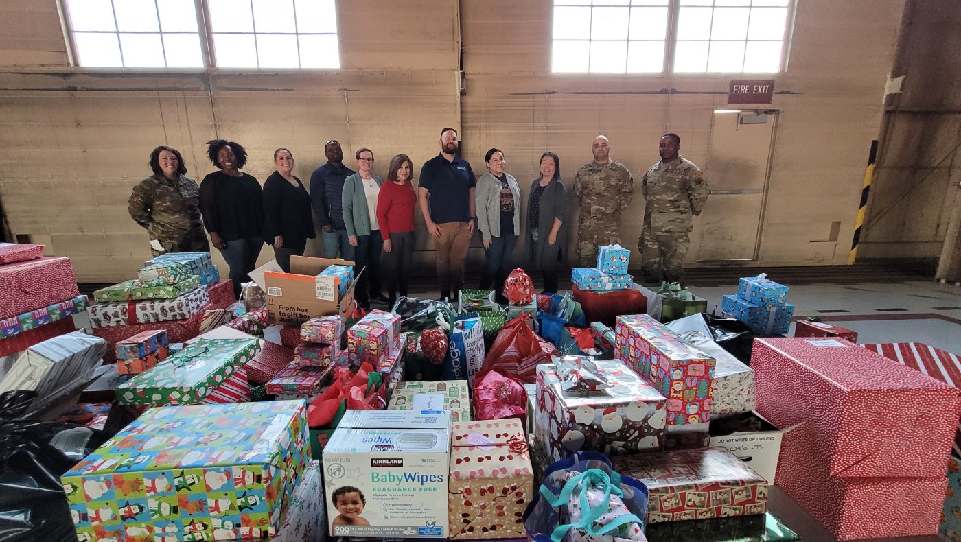 NNSS employees and U.S. Air Force personnel stand behind a table of wrapped gifts.